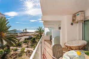 Uma varanda com vista para a praia, área de refeições com mesa e cadeiras, e unidade de ar condicionado.