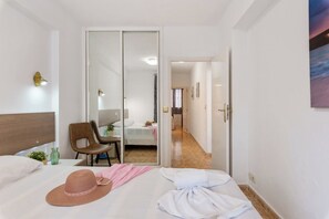 Quarto de hotel com cama, uma cadeira, escrivaninha e banheiro visível por uma porta de correr.