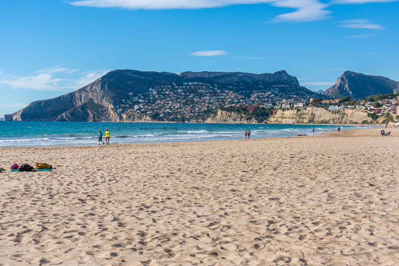 A beach with a mountain in the background and a town on the hillside.