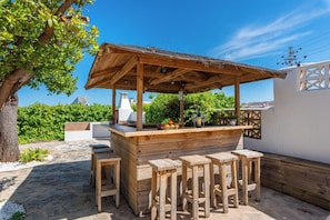 An outdoor wooden bar area with stools, a counter, and a view of the city in the background. - Villa Reva - PlusHolidays (Calpe)