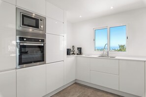 A modern kitchen with a built-in oven, microwave, and a window with a view. - Villa Reva - PlusHolidays (Calpe)