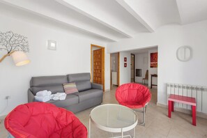 A living room with a grey sofa, red chairs, a small round table, and a radiator. - Villa Reva - PlusHolidays (Calpe)