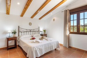 Een slaapkamer met een bed, nachtkastjes, een raam met gordijnen en een houten plafond.