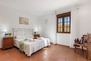 A bedroom with a bed, bedside tables, a dresser, a window with curtains, and a painting on the wall.