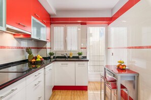 A modern kitchen with white cabinets, red accents, and a black countertop.