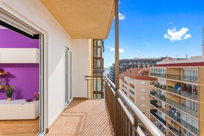 Varanda com vista para edifícios próximos, porta de correr com vidro e um pequeno espaço de estar com plantas.