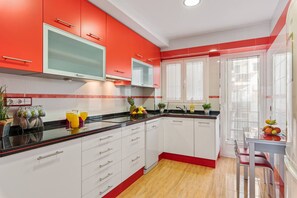 Cozinha com armários brancos, detalhes vermelhos, bancada preta e piso de madeira.