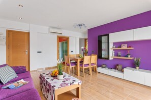 A modern living room with a purple accent wall, a dining area with wooden furniture, and a white cabinet with decorative items.