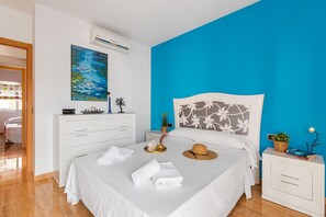 A hotel room with a bed, a bedside table, a nightstand, a dresser, a painting, and an air conditioning unit.