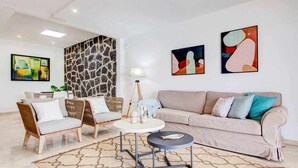 A modern living room with a beige sofa, two wicker chairs, a round coffee table, and abstract wall art. - Homo Aura. Villa with private pool in Playa Blanca (Playa Blanca (Yaiza))
