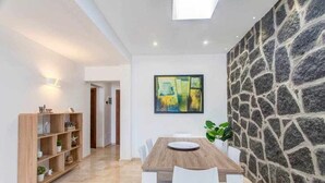 A dining area with a wooden table and white chairs, a stone wall, and a painting on the wall. - Homo Aura. Villa with private pool in Playa Blanca (Playa Blanca (Yaiza))