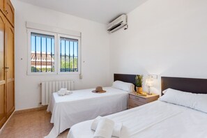 A hotel room with two beds, a window with a view, a radiator, and an air conditioning unit.