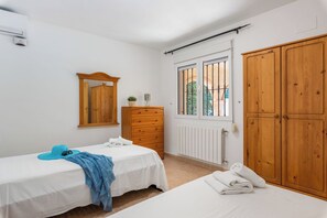 Quarto com duas camas, guarda-roupa de madeira, penteadeira e um espelho, além de janela com grades.