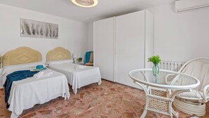 Habitación de hotel con dos camas, una mesita, una silla, un cuadro en la pared y un aire acondicionado.
