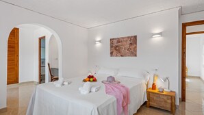 Una habitación de hotel moderna con una cama grande, una mesita de noche con lámpara y una cesta de frutas sobre la cama.