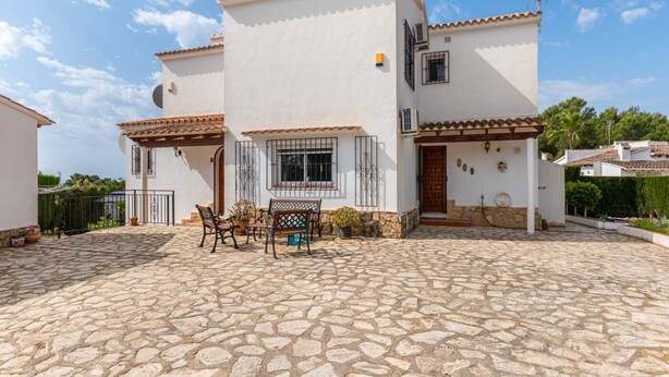 Una casa de dos pisos con un patio de piedra, mobiliario exterior y un pequeño jardín.