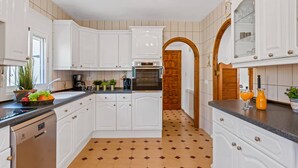 Una cocina con armarios blancos, piso de baldosas y puerta de madera.