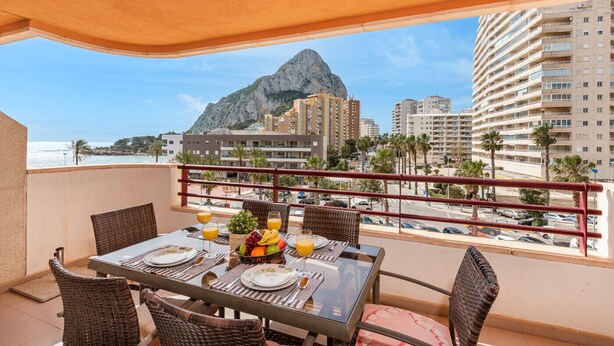 Un balcone con un tavolo apparecchiato per la colazione, affacciato su una città con una montagna imponente e palme.