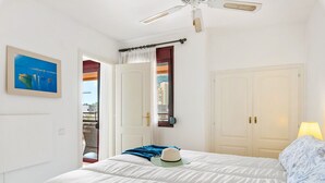 Una camera da letto con un letto, una ventola a soffitto, una finestra con tende e una porta.