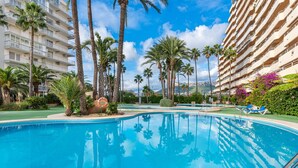 Una piscina rodeada de palmeras y un edificio hotelero de varios pisos.