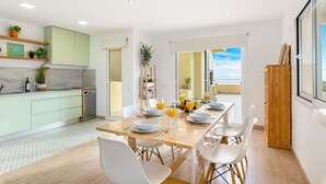 Una cocina moderna con comedor, que incluye una mesa de madera preparada para cuatro comensales, un horno empotrado y vistas al exterior.