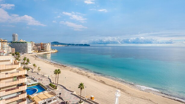 Un hotel frente al mar con vista a la playa, una piscina y un paseo marítimo con palmeras.