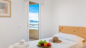 Un dormitorio con cabecera de madera, cama con ropa blanca, cesta de frutas, toalla enrollada y un sombrero sobre la cama.