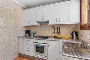 A compact kitchen with white cabinets, a built-in oven, a coffee maker, and a sink.