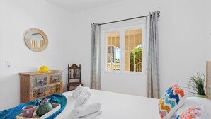 Quarto de hotel com cama, penteadeira de madeira, espelho, janela com cortinas e vista para o exterior.