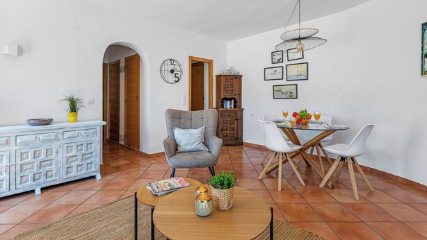 Uma sala de estar ampla com uma mesa de jantar, cadeiras, sofá e um relógio decorativo na parede.
