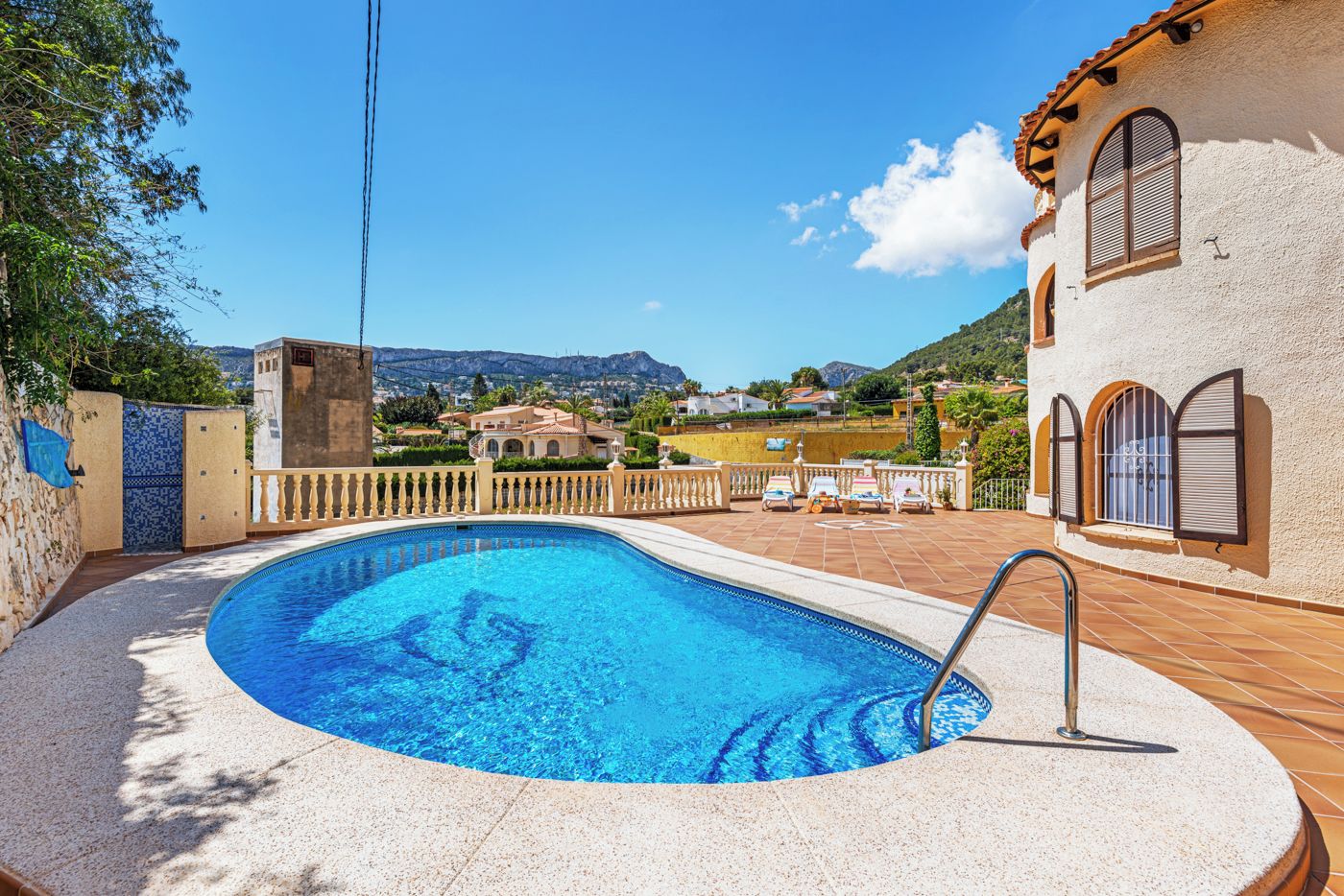 A swimming pool with a curved edge, a metal ladder, and a view of houses and mountains in the background.