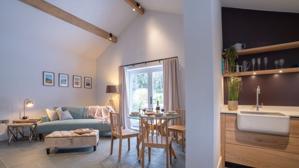 Un salon moderne comprenant un canapé, une table à manger avec des chaises, un coin cuisine avec un évier et des étagères, et une grande fenêtre avec des rideaux.