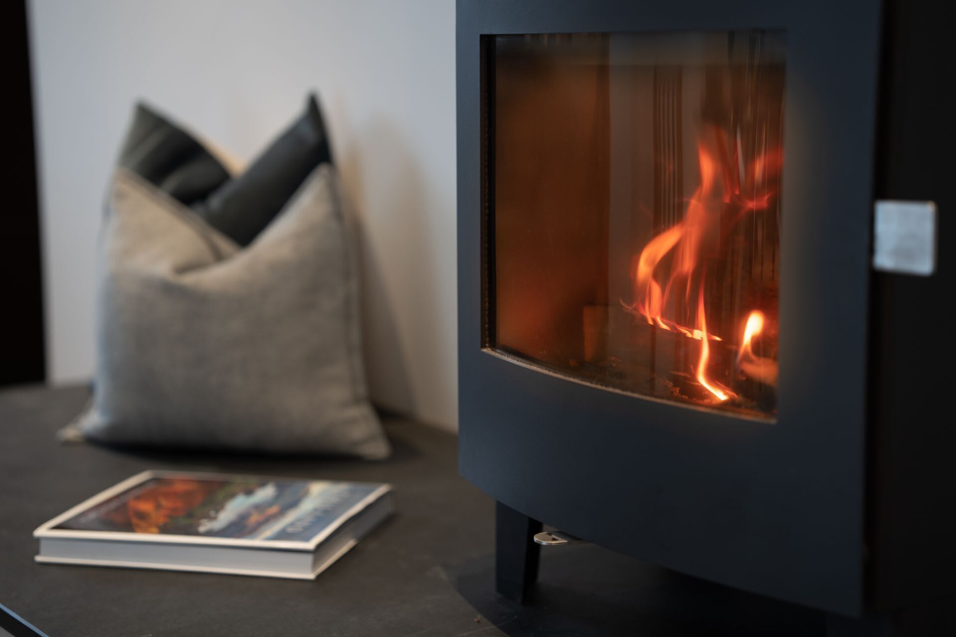 A modern fireplace with a glass front, a book, and a cushion on a dark surface.
