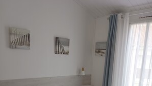 A neatly made bed with white bedding and a gray throw blanket, a white nightstand with a lamp, and two wall-mounted pictures depicting outdoor scenes.