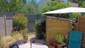 An outdoor patio with a striped tablecloth, a blue chair, a white umbrella, and potted plants.