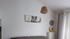 A modern living room with a grey sofa, patterned cushions, a hanging light fixture, a wall-mounted clock, and a chevron-patterned curtain.
