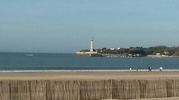 A coastal scene with a lighthouse, beach, and a wooden fence.