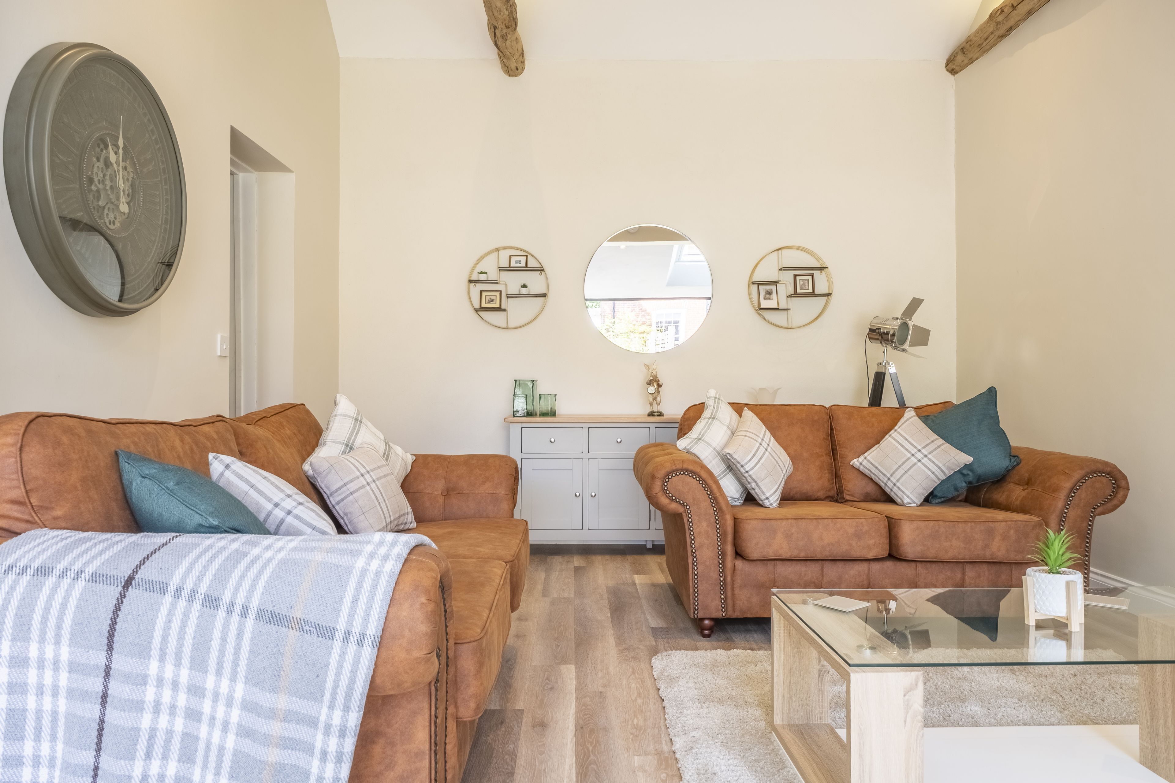 A living room with two brown leather sofas, a glass coffee table, a white cabinet, and a large mirror on the wall.