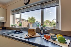 A kitchen with a large window, a sink, a cutting board with bread, a bottle of wine, and some vegetables.