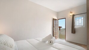 Une chambre avec un grand lit, une serviette enroulée, une porte en bois et une fenêtre.