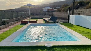 Une piscine rectangulaire à l’eau d’un bleu limpide, entourée d’une pelouse bien entretenue et d’un mur en briques.