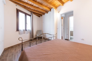 A bedroom with a bed, a chair, a window, and a door leading to another room. - Vacation Home "Casa Giovanna" with Private Terrace, Garden & A/C (San Giovanni Suergiu)