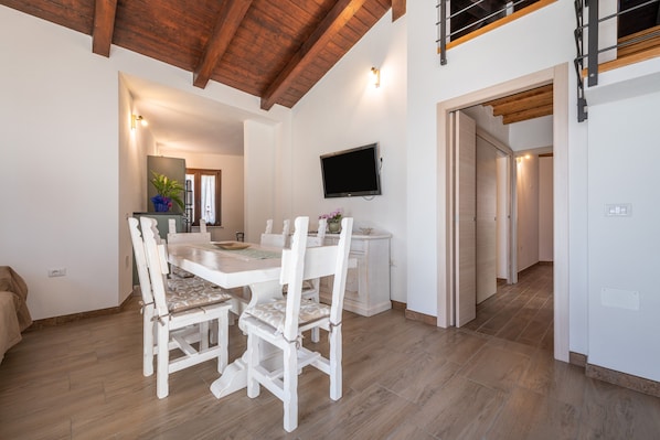 Un coin repas avec une table et des chaises en bois, un téléviseur fixé au mur et un escalier menant à un niveau supérieur.