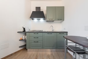 Une cuisine avec des meubles de couleur verte, une hotte noire et un évier en acier inoxydable.