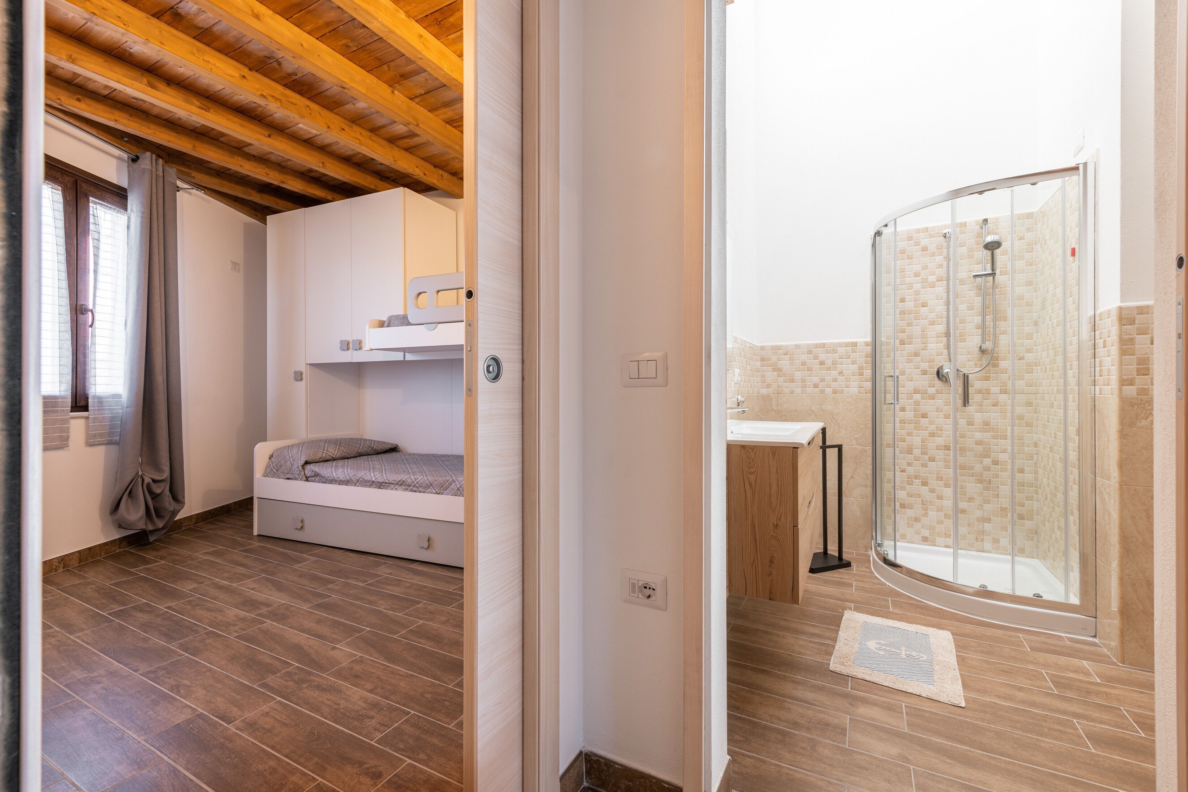 A bedroom with a bunk bed, a small bedside table, and a window with curtains.