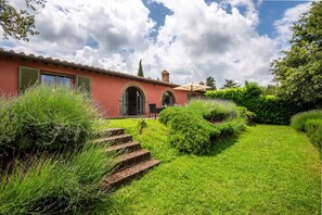 Une maison à la façade rouge, avec une cheminée et un jardin dont des marches mènent à l’entrée.