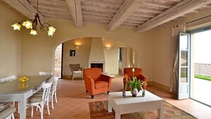 A room with a dining table, chairs, two orange armchairs, a white coffee table, and a fireplace.