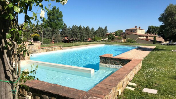 A rectangular swimming pool with clear blue water, surrounded by a stone wall and a grassy area.