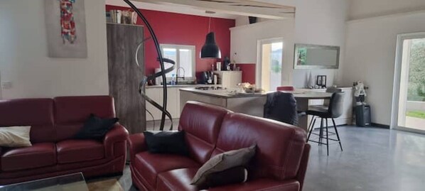 Un salon moderne avec un canapé rouge, un coin repas et une cuisine en arrière-plan.
