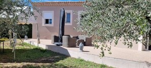 Un bâtiment doté d’un espace extérieur abrité avec des sièges, d’une petite fenêtre et d’un arbre aux feuilles vertes.